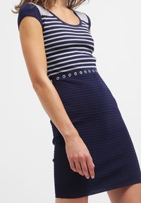 Robe rayée marine à manches courtes, présentant un motif à rayures horizontales argentées et marines, une texture côtelée et des œillets métalliques décoratifs à la taille.