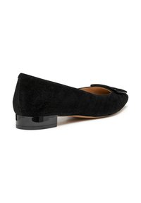 Zapato plano de ante negro con un tacón bajo y brillante negro y un acento decorativo de moño en la puntera. Textura suave y diseño de punta afilada.