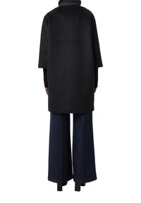 Cappotto in misto lana nero con maniche larghe, design lungo fino al ginocchio, abbinato a jeans in denim blu scuro a gamba larga, con una leggera texture.