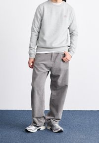 Světle šedá mikina, kulatý výstřih, žebrované manžety. Volné šedé kordové kalhoty. Stříbrné a černé sportovní tenisky. Jednoduché pozadí.