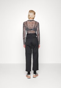 Black high-waisted trousers paired with a sheer long-sleeve top featuring a blue and white wavy pattern. The outfit is completed with athletic shoes.
