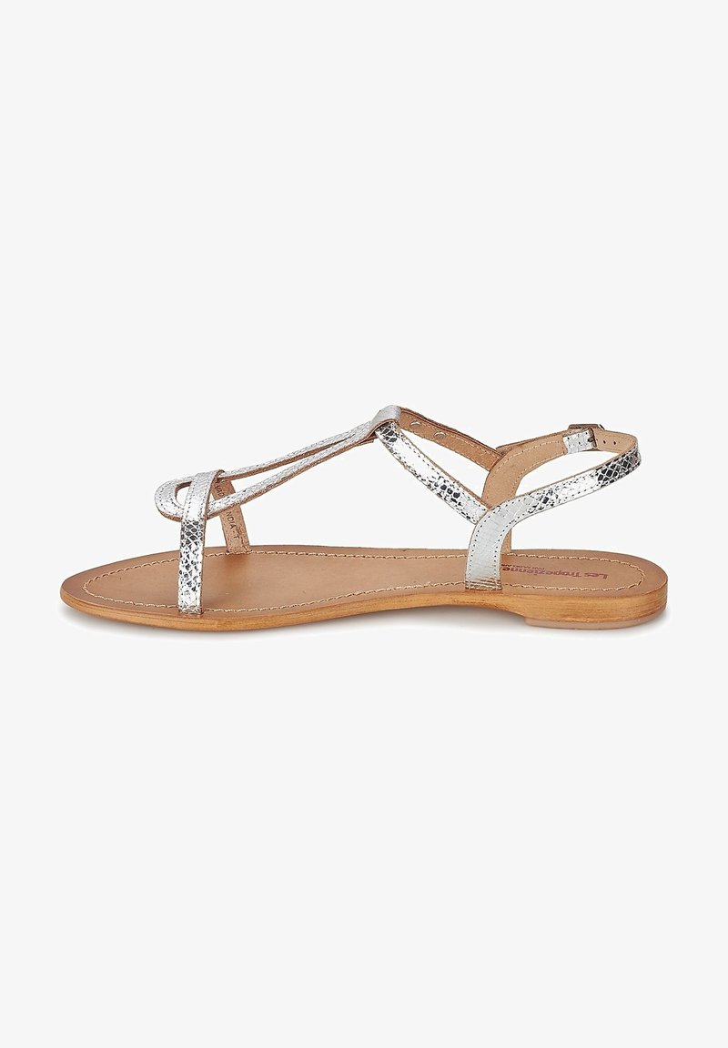 Zilveren metalen platte sandalen met gekruiste banden, een leren binnenzool en een lichtbruine platte zool. Eenvoudig ontwerp met minimale details.