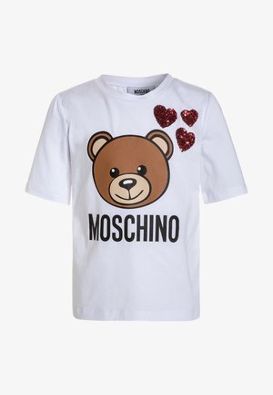 Biała koszulka z krótkim rękawem z grafiką brązowego niedźwiedzia, czarnym napisem "MOSCHINO" oraz trzema czerwonymi cekinowymi sercami na górnej lewej części.