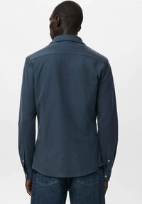 Camisa tejida azul marino con cuello extendido, mangas largas y puños abotonados, con una tela texturizada y un dobladillo ligeramente curvado.