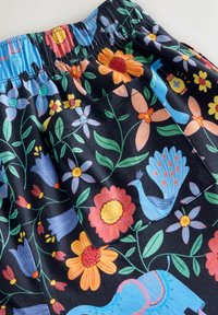 Dunkler Stoff mit buntem Blumenmuster, einschließlich orangefarbener, blauer und gelber Blumen, grünen Blättern, einem blauen Elefanten und einem blauen Pfau in der Nähe einer Tasche.
