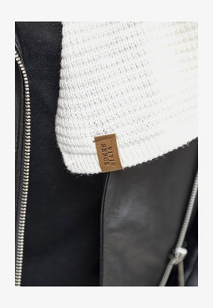 Black leather jacket partially visible with a knitted white collar. Features a brown tag labeled "VIVI SENCE." Zipper detail shown.