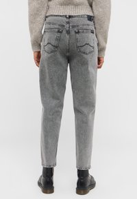 Jasnoszare dżinsy o luźnym kroju, lekko zwężane nogawki oraz dwie tylne kieszenie z zaokrąglonymi szwami. Noszone z czarnymi botkami.