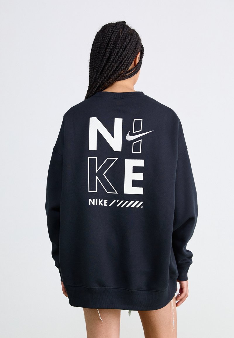 Svart oversized sweatshirt med vit "NIKE" grafisk design och logotyp på baksidan, tillverkad av mjukt tyg med ribbade ärmslut och fåll.