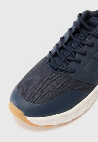 Navy blue athletic shoe with mesh fabric and rubber sole. Features rounded toe, lace-up design, and textured accents on the upper surface.