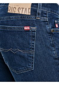 Sötétkék farmernadrág hátsó zsebében piros Big Star márkajelzésű címkék és a derékrészen beigeszínű bőrből készült folt varrva.
