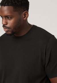 T-shirt noir en coton avec un col rond, des manches courtes et une texture lisse, présenté en vue de profil en gros plan.