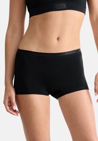 Musta puuvillaiset poikashortsit, joissa on sileä vyötärönauha, saumattomat sivut ja istuva muotoilu mukavuutta varten. Yksityiskohtina on minimaaliset ompelut.