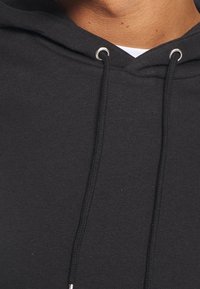 Sudadera con capucha negra de textura suave, con un bolsillo frontal y ojales plateados para los cordones.