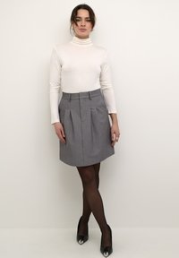 Jupe plissée grise taille haute, accompagnée d'un pull à col roulé blanc. Le tout est complété par des escarpins noirs à talons hauts avec un embout métallique.