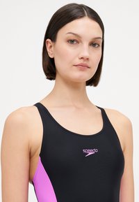 Svart badedrakt med rosa sidepanel og logo. Glatt tekstur, atletisk design med brede stropper og scoop-nakkeåpning. Passer for vannaktiviteter.