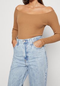 Brown ribbed off-shoulder long-sleeve top paired with high-waisted light blue denim jeans. Jeans feature front pockets and a zipper closure.