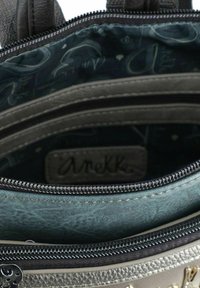 Interior de una bolsa gris con un forro texturizado de color azul claro, que presenta múltiples compartimentos, cierres con cremallera y una etiqueta de marca visible.