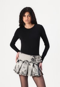 Un haut à manches longues noir associé à une jupe courte plissée en denim gris décoloré, dotée de trois boucles métalliques en accent et d'une finition texturée.