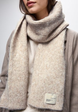 Sciarpa lavorata a maglia beige con texture a costine, morbida miscela di lana, con un'etichetta su un'estremità con la scritta "PARA STREET ONE" in testo nero.