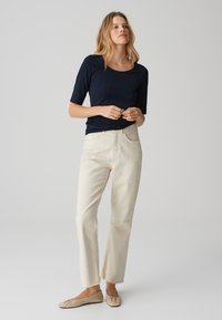 Top blu navy a maniche corte, pantaloni dritti color crema con orlo sfrangiato e ballerine beige. L'outfit presenta un design semplice e materiali morbidi.