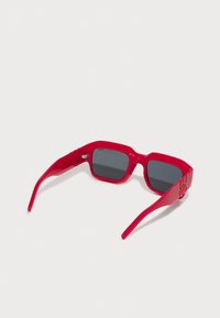 Red plastic sunglasses with square frames, dark lenses, and logo on side, featuring a glossy finish and sleek design.
