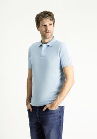 Polo de manga corta azul claro en una suave mezcla de algodón, con collar, tapeta de dos botones y un diseño ajustado, combinado con jeans de mezclilla.