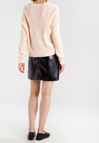 Hellrosa gestrickter Pullover mit langen Ärmeln, kombiniert mit einem hoch taillierten schwarzen glänzenden Lederrrock, der eine glatte, glänzende Textur zeigt.