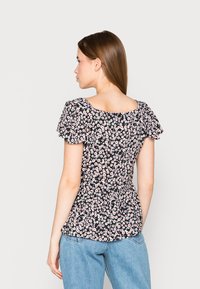 Top peplum floral com base preta, flores brancas e cor-de-rosa, mangas curtas bufantes, decote quadrado e detalhe de cintura franzida. Combinado com jeans azuis.