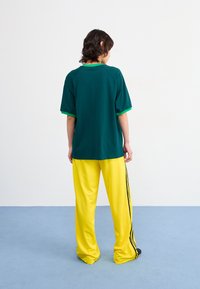 Green short-sleeve top with a contrasting green neckline paired with loose, yellow pants featuring black side stripes.