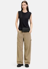 Schwarzes geripptes ärmelloses Oberteil, beiger weit geschnittener Hosenanzug und eine elegante schwarze Umhängetasche mit strukturiertem Finish, ausgestattet mit einem einfachen Reißverschluss.