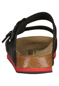 Black sandal with an adjustable strap, cork footbed, and a reddish-black rubber sole. Features a textured heel and minimalistic design.