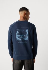 Marineblå crew neck sweatshirt med et grafisk landskapsdesign med trær og tekst på baksiden. Ribbet mansjetter og hem. Myk stoff.