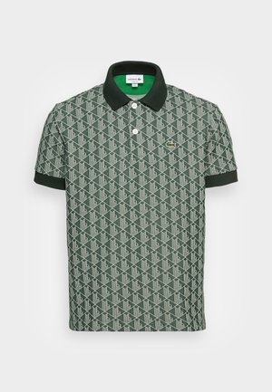 Polo vert à manches courtes avec motif géométrique, col et poignets noirs, deux boutons blancs et petit logo crocodile sur la poitrine.