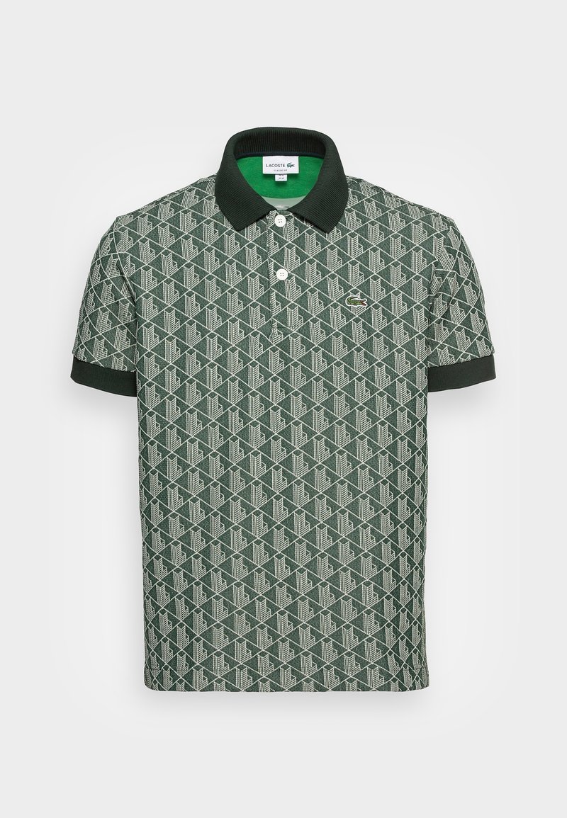 Polo vert à manches courtes avec motif géométrique, col et poignets noirs, deux boutons blancs et petit logo crocodile sur la poitrine.