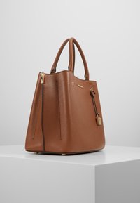 Brązowa skórzana torebka z teksturowanym wykończeniem, zwężającym się kształtem, podwójnymi uchwytami, złotymi detalami oraz akcesorium w formie zamka.