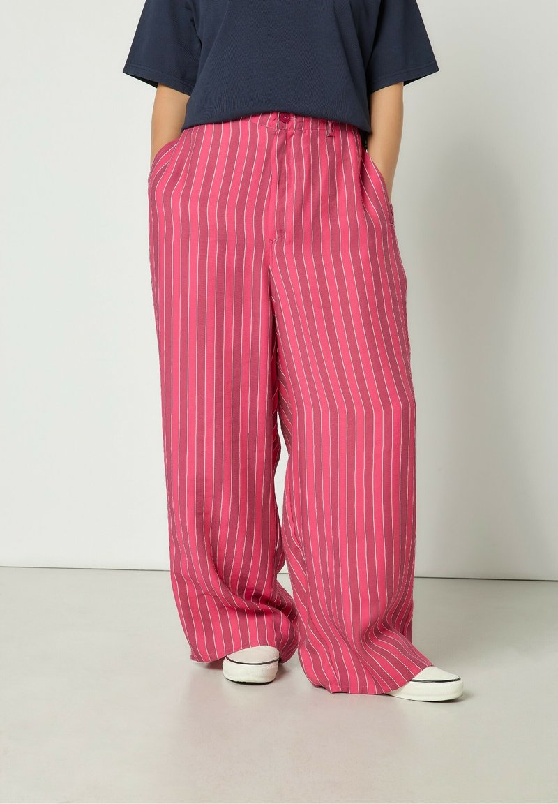 Ružičaste prugaste široke hlače napravljene od lagane tkanine, sa dva bočna džepa i opuštenim krojem. Naglašene vertikalnim bijelim prugama.