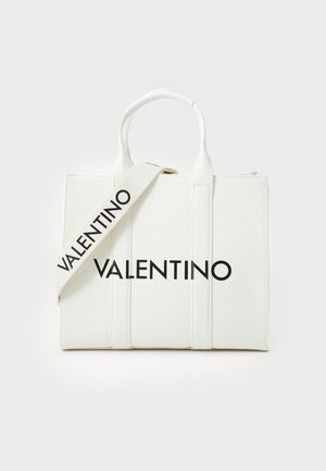 Sac en toile blanc avec le mot "VALENTINO" en lettres noires audacieuses, anses supérieures doubles et une bandoulière détachable. Forme rectangulaire avec des coutures verticales.