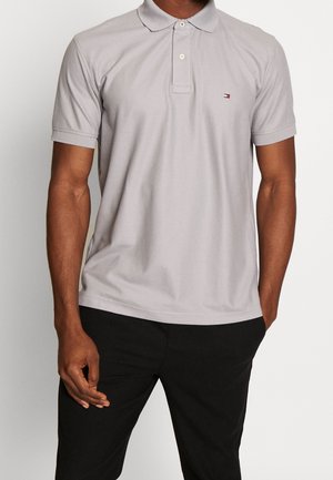 Lysegrå polo i bomuld med klassisk krave, korte ærmer og et lille logodetalje på venstre bryst. Båret med sorte bukser.