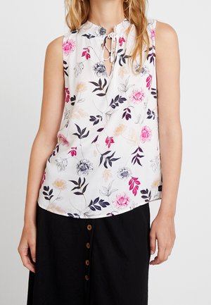 Ærmeløs hvid bluse med pink, beige og sort blomstermønster, nøglehulshalsudskæring med bindebånd, båret med sort nederdel med høj talje og knapper.