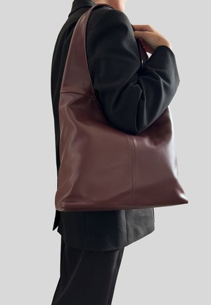 Bordová kožená taška přes rameno s hladkým povrchem, velkým rozměrem a minimalistickým designem. Prošívané detaily podél švů.