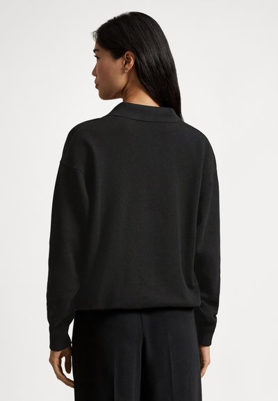 Črni pleteni pulover z ovratnikom, širokim krojem in rebrastimi manšetami. Gladek tekstura z minimalističnim dizajnom.