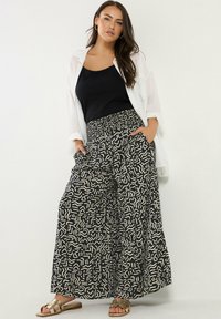 Svarta vida byxor med ett vitt abstrakt mönster, med en smockad midja och sidofickor. Matchas med en svart linne och sandaler.