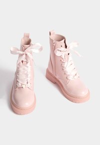 Botines de charol rosa con cordones de cinta de satén, cremalleras laterales y suelas texturizadas. Punta redondeada y tiradores para facilitar el calzado.