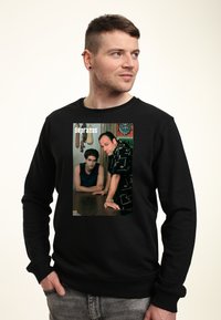 Černá mikina se grafickým potiskem dvou postav z pořadu, na pozadí s indoorovým prostředím.