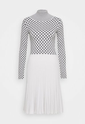 Vestido de manga larga con parte superior de cuadros en blanco y negro y falda plisada blanca sobre un fondo liso.