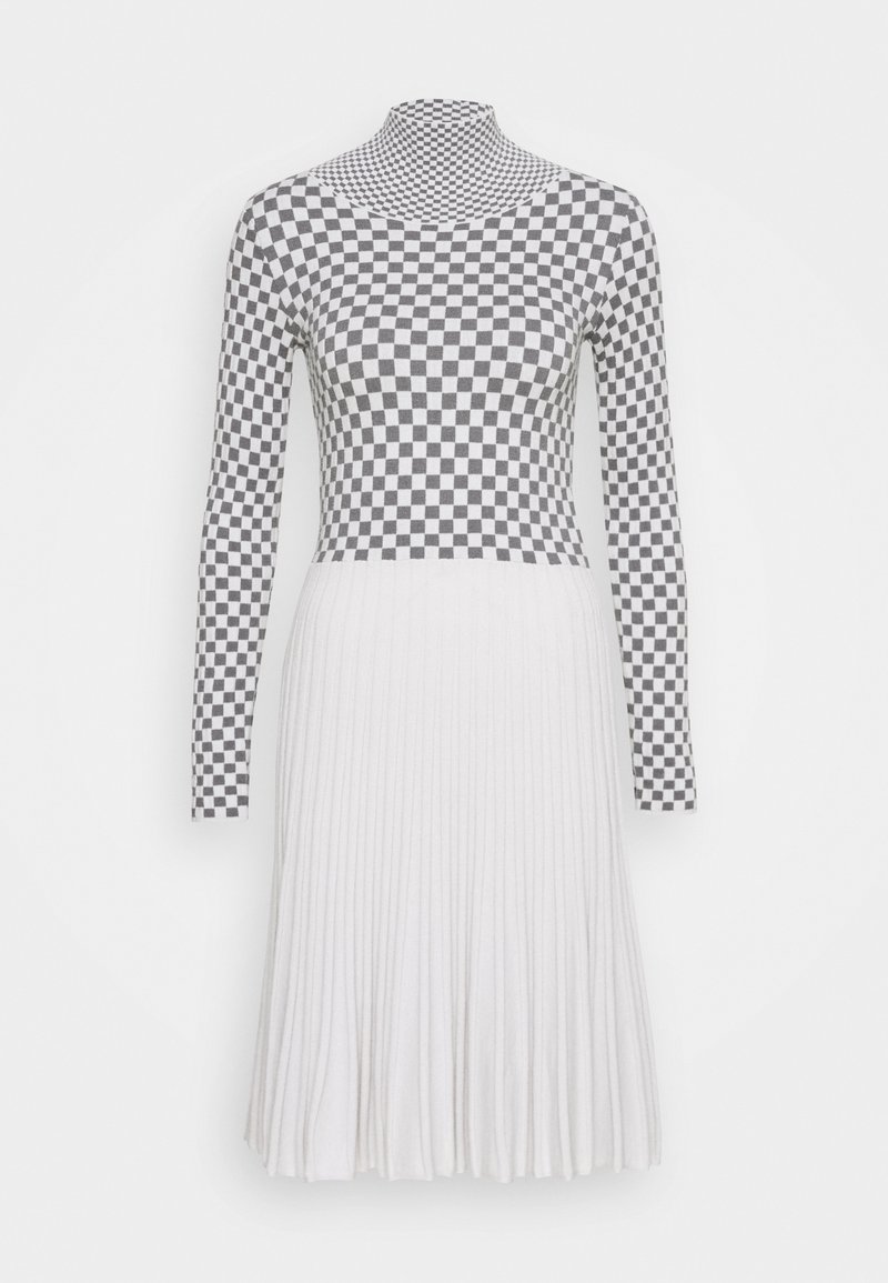 Robe à manches longues avec un haut à carreaux noirs et blancs et une jupe plissée blanche sur un fond uni.