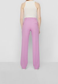 Pantalones de pierna ancha rosa con una textura suave, que cuentan con un bolsillo trasero, estilizados con una camiseta sin mangas blanca ajustada. Cintura visible y líneas limpias.