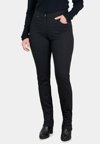 Pantalones negros con un patrón texturizado, diseño ajustado, bolsillos delanteros y cierre de botón, combinados con botas de tacón negras.