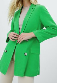 Groene linnen blazer met een getailleerde pasvorm, dubbele knoopsluiting, rever met inkeping, twee voorzakken en grote grijze knopen.