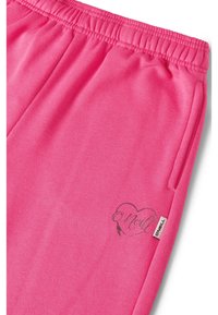 Roza trenirke z elastičnim pasom. Na strani ima srebrno srčne logo in oznako. Mehka tkanina z gladko teksturo.